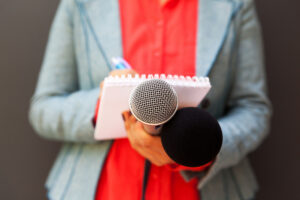 Female reporter at news conference, writing notes, holding microphone