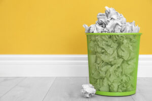 Metal bin with crumpled paper against colour wall
